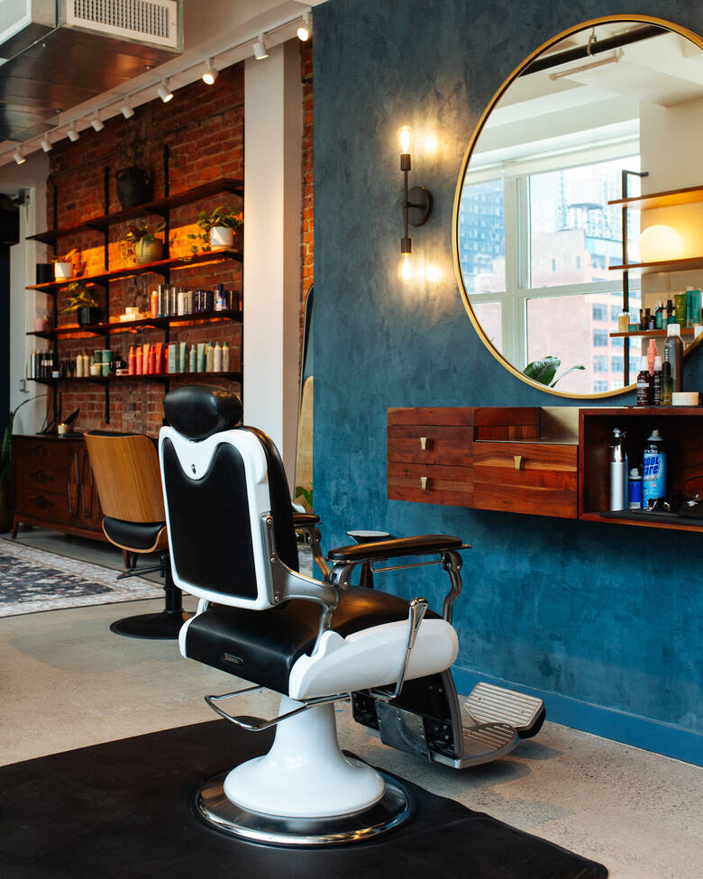 A vintage barber chair facing a round brass mirror and deep blue plaster wall at Clubhouse