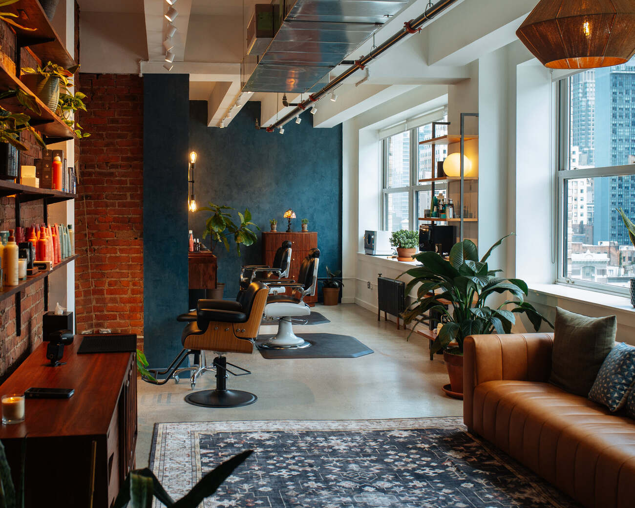 The sunlit Clubhouse studio with barber stations, exposed brick, plants, and Manhattan windows